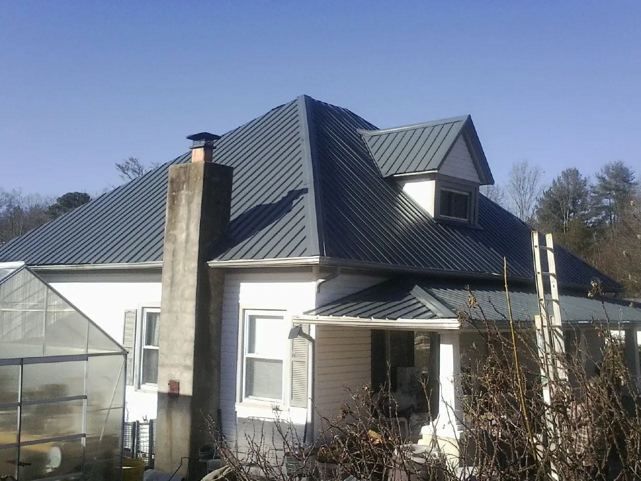 Dark blue standing seam metal roof on a white farmhouse with dormer — Slate & Tile Roof Repair by Roofing Brothers in Ellsworth