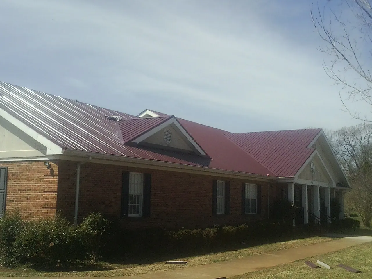 Red metal roof with gabled entries on a long brick building, from a Hail Damage Roof Repair job in Ellsworth