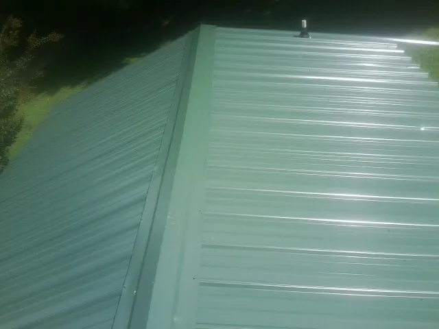 New green metal panels meeting at the ridge of a roof — Flat Roof Repair work by our crew in Ellsworth
