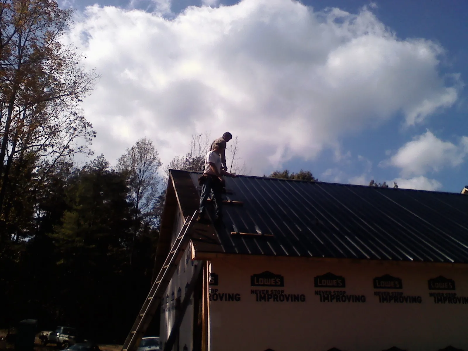 Roofer fastening dark metal panels high against a cloudy sky, from a Roof Inspection job in Ellsworth